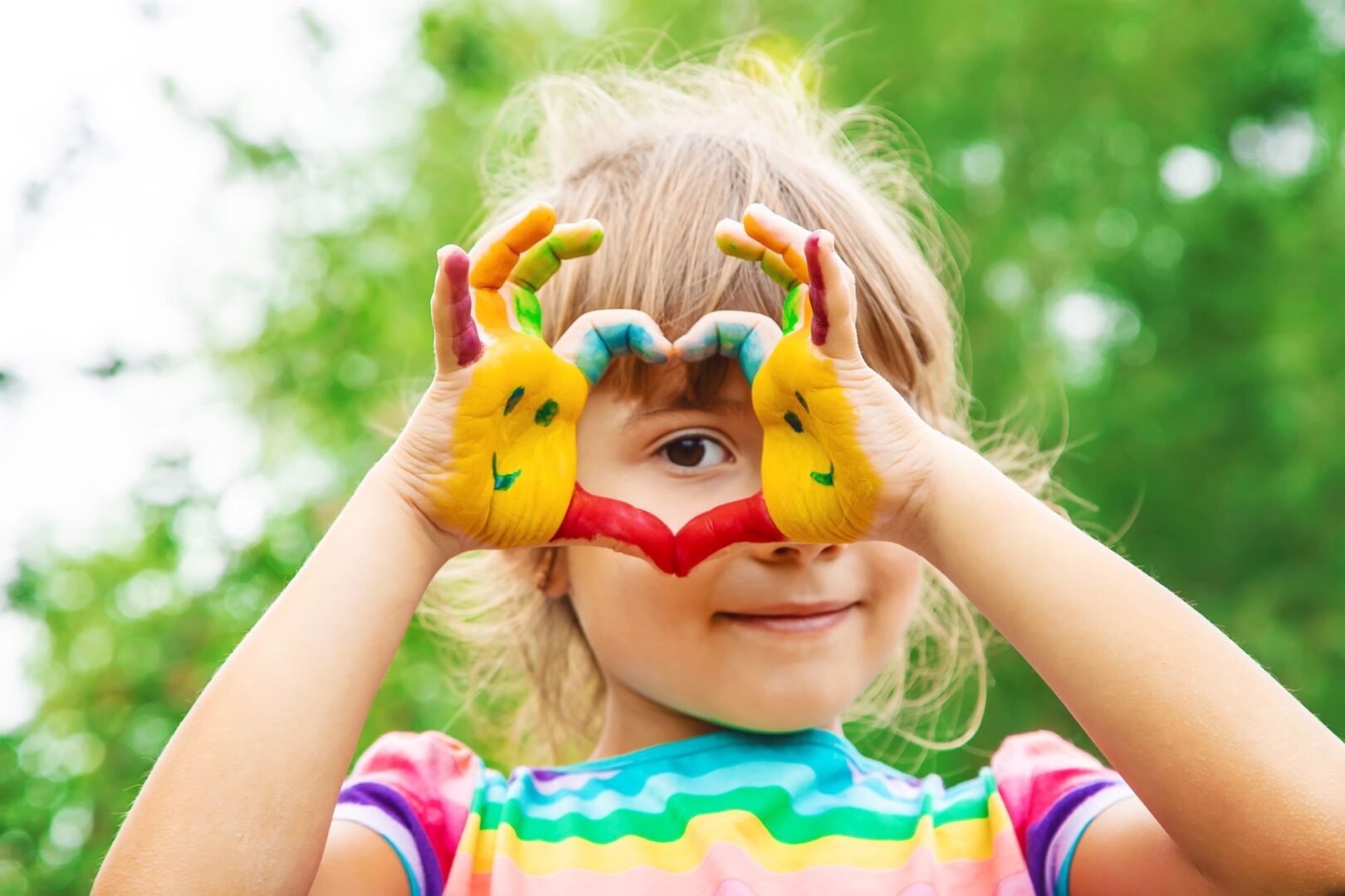 A little girl with painted hands making a heart.