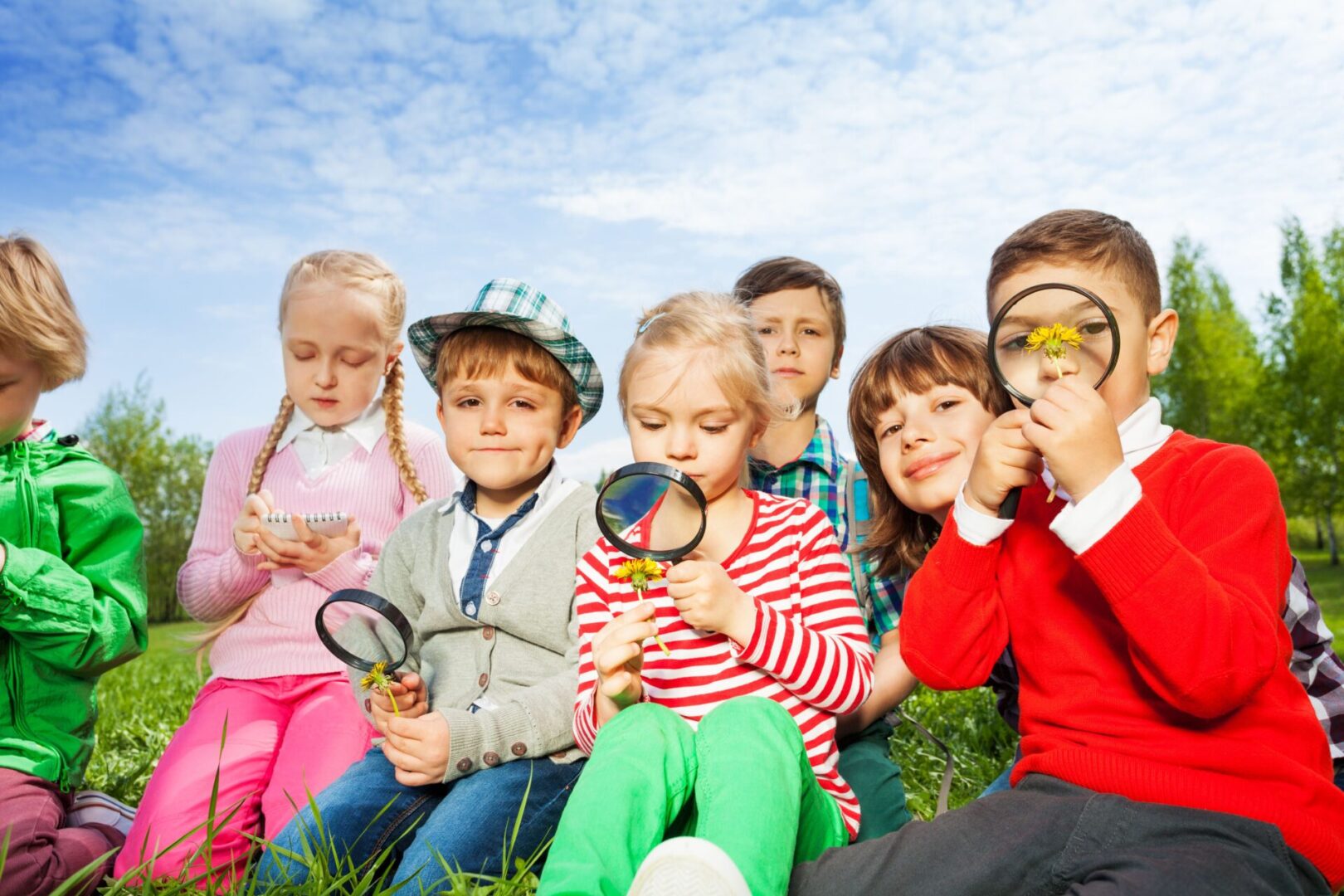 A group of children sitting in the grass with magnifying glasses.